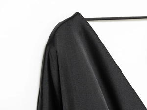 Close-up of the silk-like draped shoulder of a black satin dress on a hanger
