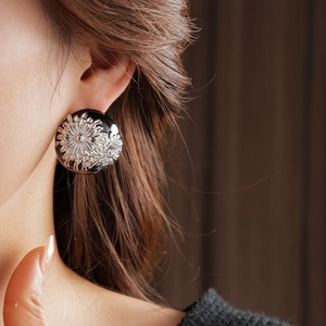 Close-up of vintage black round earrings with silver daisy floral relief on model's ear