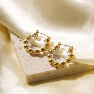 Detail of wavy golden hoop earrings with white pearls on a silk fabric background