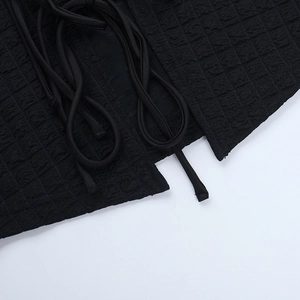 Macro shot of black textured waffle fabric with detailed lace-up tie on long sleeve top