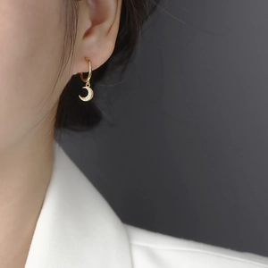 Elegant gold moon earrings with small crystals worn on a model against dark background