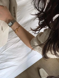 Detailed look of a gold knot bracelet and square roman dial watch on a female wrist