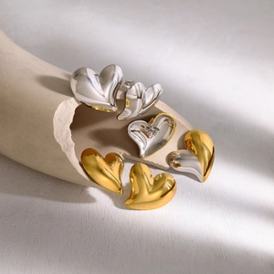 Minimalist heart-shaped 18K gold and silver earrings on artistic ceramic background