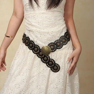 Detail of western punk black leather belt with bronze rivets and large carved round buckle