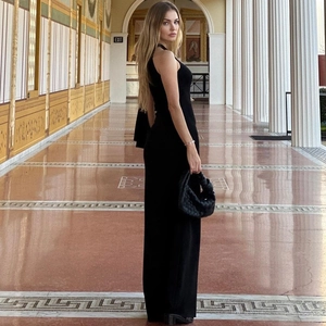 Detail of elegant black one-shoulder slim maxi dress with woven handbag in corridor