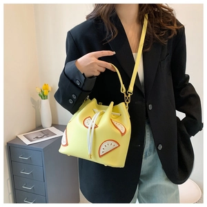 Yellow lemon drawstring bucket bag styled on a model with a long shoulder strap
