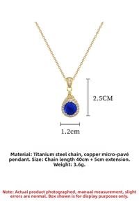 Close-up of teardrop pendant with blue gemstone and micro-pave crystals on gold chain