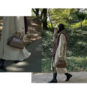 Detail of round brown leather handbag with double handles shown in outdoor park setting