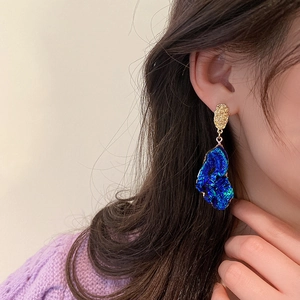 Close-up of irregular blue resin pendant earrings with textured golden studs on a model