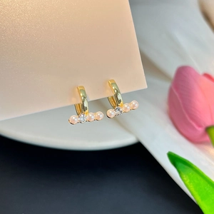 Détail de créoles dorées avec perles et cristal central sur une carte rose