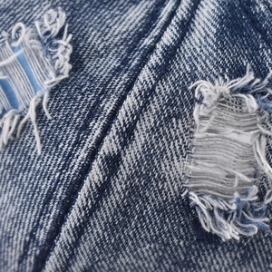 Detail of washed denim texture featuring distressed holes and frayed raw edges on the cap
