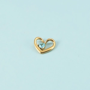 Détail d'un pendentif cœur doré serti d'un cristal bleu clair sur fond bleu clair
