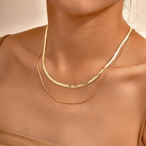 Close-up of a double-layered gold snake bone necklace worn on a woman's collarbone