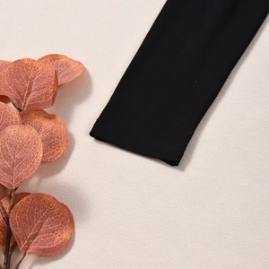Close-up of black long sleeve cuff with double-stitched hem on a beige textured surface