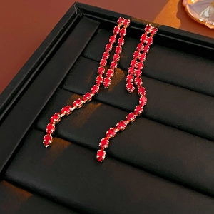 Detail of long gold earrings with red rectangular gemstones on a black jewelry stand