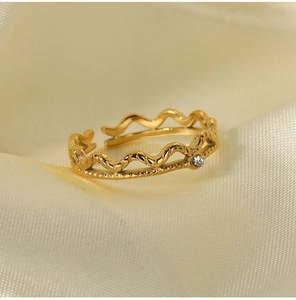 Close-up of wave-shaped gold open ring featuring a single sparkling zircon setting