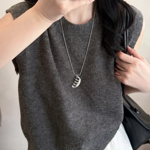 Collier minimaliste à pendentif peigne argenté sur un pull en maille grise pour femme