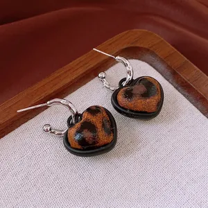 Retro heart-shaped leopard print drop earrings with silver pins on a wooden display