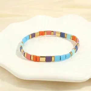 Detail of colorful enamel tile bracelets with gold accents on a ceramic plate