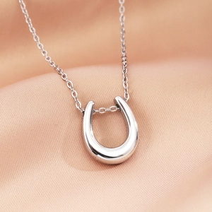 Elegant silver U-shape pendant necklace on satin background with fine metal cross chain
