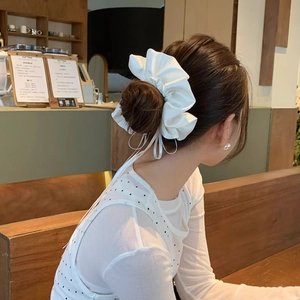 Detail view of large white satin bow scrunchie with long ribbons on blonde hair