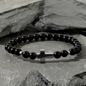 Detailed shot of black matte agate beads and silver cross charm on a grey stone slab
