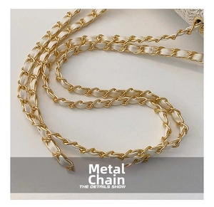 Detail of golden metal chain interwoven with white leather on a straw handbag