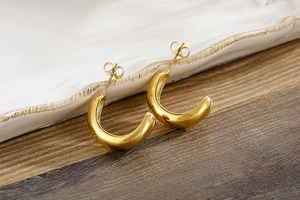 Detailed view of chunky gold-plated C-shaped earrings on a rustic wooden and ceramic base
