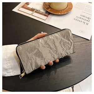 Close-up of a long silver crinkled velvet wallet with gold zipper and stylish lifestyle props