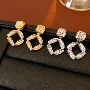 Detail of square gold and silver pearl drop earrings on a black jewelry tray
