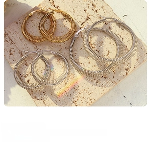 Three sizes of gold and silver spring coil hoop earrings on a textured stone slab