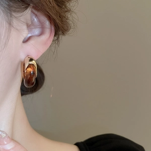 Close-up of a model wearing C-shaped resin earrings in amber and gold finish