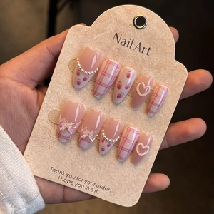 Detail of pink almond fake nails featuring strawberry print, plaid patterns and 3D bows