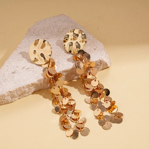 Detail of gold metal fringe earrings with textured discs on a natural stone background