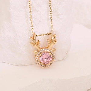 Elegant gold reindeer antler necklace with a round pink zircon on white stone surface