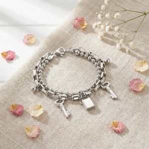 Close-up of double-layered stainless steel bracelet with lock and key charms on linen