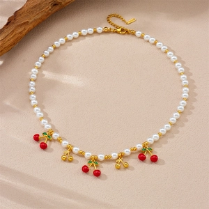 Charmant collier de perles et billes dorées avec pendentifs cerises sur fond de sable