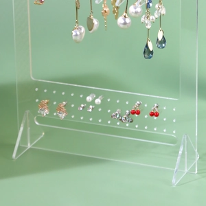 Close-up of clear acrylic earring holder with multiple holes displaying jewelry pieces