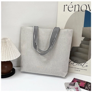 Detailed view of canvas tote bag with black and white striped handles in lifestyle setting