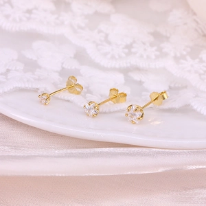 Macro shot of three gold star stud earrings with clear gems on white lace fabric