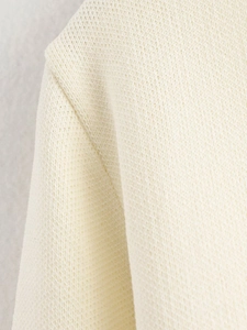 Detailaufnahme von cremefarbenem Strickstoff mit feinen Nähten und weicher Textur
