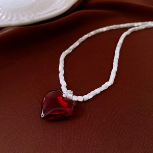 Detailed shot of a red heart pendant necklace with white opal beads on brown velvet