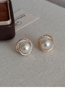 Detail of round pearl stud earrings with zircon halo on beige linen background
