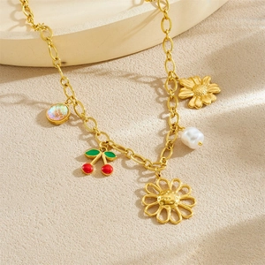 Collier doré avec breloques cerise, marguerite et perle présenté sur un plateau rond
