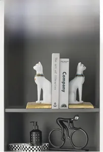 Detail of matte white Egyptian cat bookends with blue gold collars on a modern bookshelf