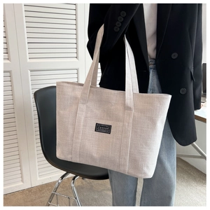 Close-up of beige canvas tote bag showing textured fabric and stylish brand patch