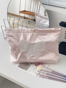 Detail of pink satin makeup bag with white bow embroidery and pearl zipper puller