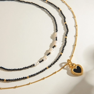 Three-layer stacked necklace featuring black beads, pearls, and golden heart pendant