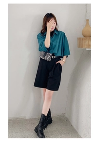 Detail of dark teal short sleeve shirt with STUDIO embossed lettering and black shorts