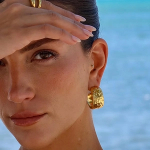 Close-up of hammered texture 14K gold C-shaped hoop earrings on model at beach
